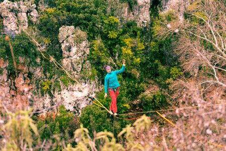 A woman is walking along a stretched sling. Highline in the mountains. Woman catches balance. Performance of a tightrope walker in nature.の写真素材