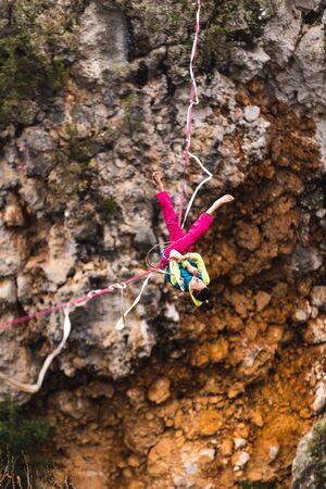 girl falls on a stretched sling. Highline in the mountains. woman lost her balance. Speech tightrope walker in nature. Highliner hanging on a rope. Fall athlete.の写真素材