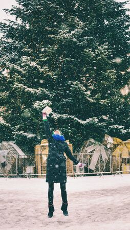 Woman with a Christmas present near a decorated city tree. The girl walks along the snow-covered street. Brunette in winter clothes rejoices at a New Year's gift. Winter holidays.の写真素材