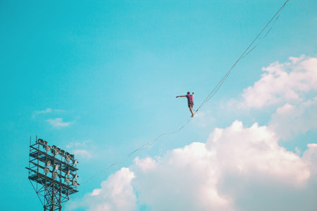 Highliner on the background of blue sky makes a move. A man is walking along a stretched sling....
