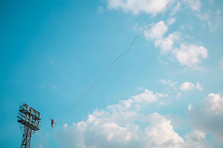Highliner on the background of blue sky makes a move. A man is walking along a stretched sling. Performance tightrope walker. Man balances over the abyss. A decisive step forward.の写真素材