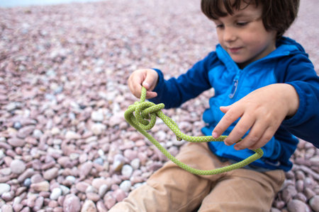 A child learns to knit a knot from a rope. A little boy is trying to tie a knot. Scout training....