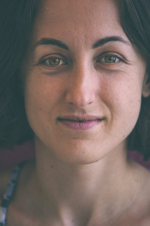 Portrait of a young woman. Face close up. Skin with age spots. Brunette with green eyes.