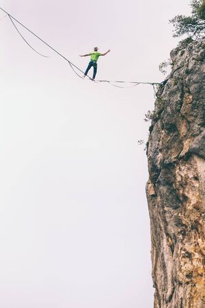 Highline on the background of the mountains makes a step. A man is walking along a stretched sling. Performance of a tightrope walker. Highliner balances over the abyss. Highline between two rocks.の写真素材
