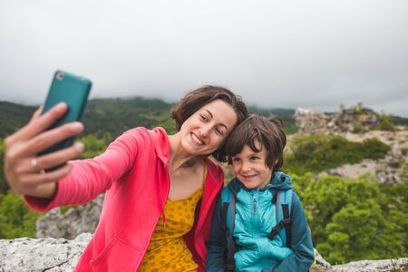 A woman takes a selfie with her son on top of a mountain. The boy is photographed with his mother. Traveling with children. A child walks in the park with his mother.の写真素材