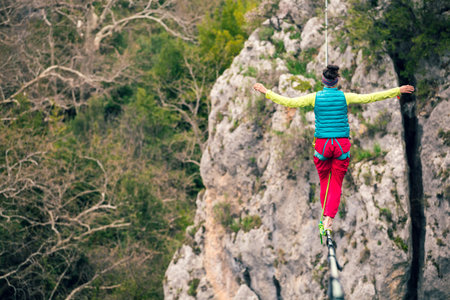 A woman is walking along a stretched sling. Highline in the mountains. Woman catches balance....