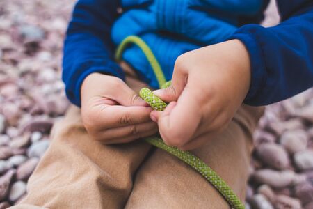 A child learns to knit a knot from a rope. A little boy is trying to tie a knot. Scout training. Children's hands and safety rope.の写真素材