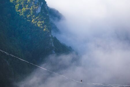 a man walks along a stretched sling high above the clouds. highliner catches the balance on a long and high sling pull in a canyon. Extreme sports in Bosnia and Herzagovina,の写真素材