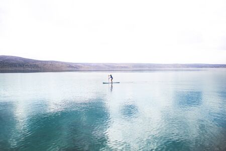 Young attractive woman kayaking, SUP, in the blue waters of the sea. a lonely girl stands on a board in the middle of a strait in the Adriatic Sea of Croatia. active life concept.の写真素材
