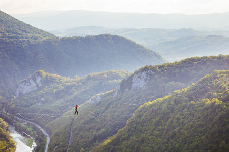 A man is walking along a stretched sling. Highline in the mountains. Man catches balance....