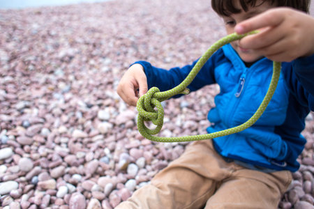 A child learns to knit a knot from a rope. A little boy is trying to tie a knot. Scout training. Children's hands and safety rope.の写真素材