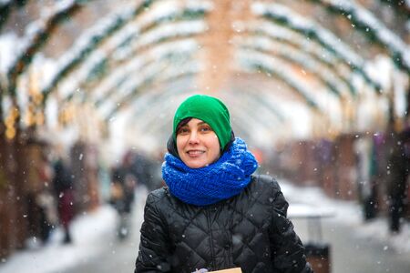 Woman on a city street during a snowfall. Winter holidays. Town in a festive decoration. Christmas holidays. New Year. Decorated street. Smiling girl walks around the city.の写真素材