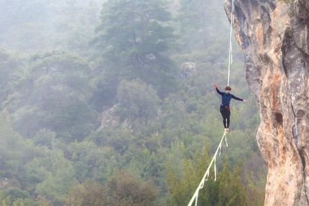 A woman is walking along a stretched sling. Highline in the mountains. Woman catches balance....