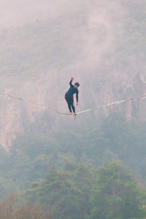 A woman is walking along a stretched sling. Highline in the mountains. Woman catches balance....
