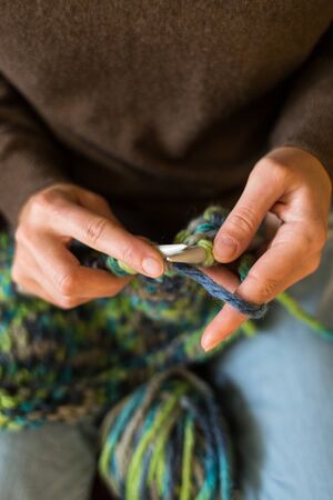 A woman knits from thick yarn. Handmade clothes. The girl sits on the couch and goes in for her hobbies. Knitting close up. Knitting needles.の写真素材