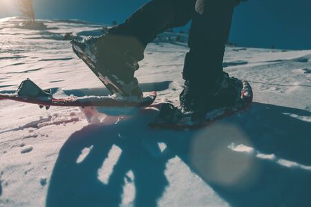 A man in snowshoes. Equipment for winter hiking in the mountains. Feet on the snow close-up. Active lifestyle. Journey in the mountains in winter. Extreme vacation in nature.の写真素材