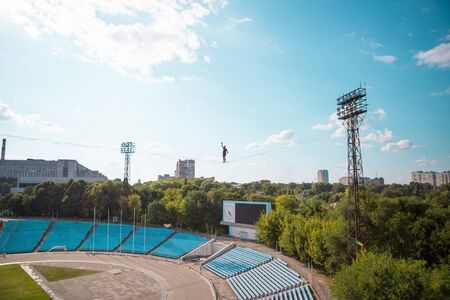 Highliner goes over the stadium. A man walks along a stretched sling over the city. Ropewalker catches the balance. The development of a sense of balance. Highline in the city.の写真素材