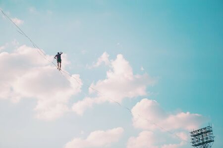Highliner on the background of blue sky makes a move. A man is walking along a stretched sling. Performance tightrope walker. Man balances over the abyss. A decisive step forward.の写真素材