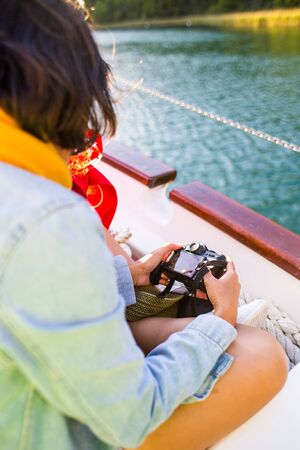 Traveling on a rented boat. A woman is sailing and taking pictures. A girl sits on board a ship and holds a camera in her hands. River tour.の写真素材