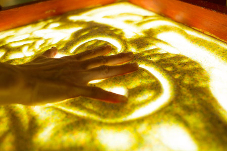 Drawings in the sand. Art therapy. Sand animation. Female fingers draw a heart in the sand. The development of the imagination. Patterns. Backlit table.の写真素材