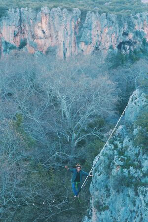 A man is walking along a stretched sling. Highline in the mountains. Man catches balance. Performance of a tightrope walker in nature. Highliner on the background of the mountains.の写真素材