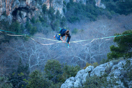 A man is walking along a stretched sling. Highline in the mountains. The man has lost balance....