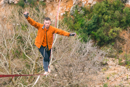 A man is walking along a stretched sling. Highline in the mountains. Man catches balance....