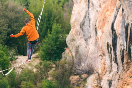 A man is walking along a stretched sling. Highline in the mountains. Man catches balance....