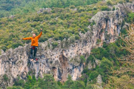 A man is walking along a stretched sling. Highline in the mountains. Man catches balance. Performance of a tightrope walker in nature. Highliner on the background of the mountains.の写真素材