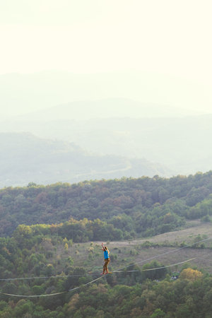 A man is walking along a stretched sling. Highline in the mountains. Man catches balance....