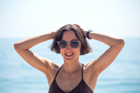 A smiling woman is standing on the seashore. Slender girl resting on the ocean. A brunette stands on...