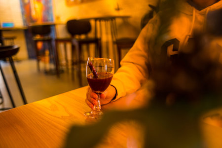 Woman holds a glass of mulled wine. Cinnamon stick in wine. A glass in female hands. The girl is...