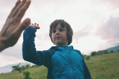 A boy climbed to the top of the mountain and gives five. Traveling with children. The child holds...