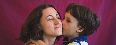 Cute boy kisses and hugs mom. Portrait of a woman with a child. The brown-eyed boy whispers to mom in the ear.の写真素材