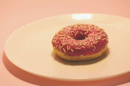 Donut with pink icing on a white plate. Fatty sweetness. Tasty cake. Round cookies.の写真素材