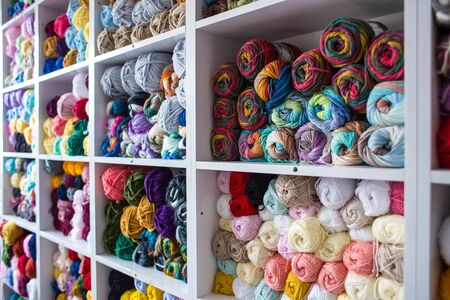 Rack with yarn in the store. Shelf with multi-colored threads for knitting. Background from colored yarn. Balls of thread close-up. Materials for needlework. の写真素材