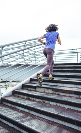 A woman runs up the stairs. Running training in the city. Jogging. Reaching the goal. The desire for...