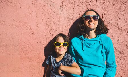 A woman with her son sits against a pink wall. Portrait of a boy with mom. A smiling child spends time with his mother. Toddler hugs mom.の写真素材