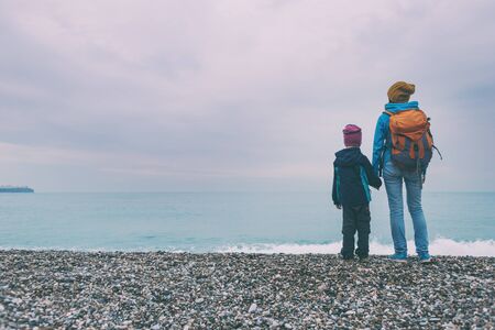 A woman and a child walk along the seashore on a rainy autumn day. Boy with mom come into the sea. Ocean and sky with clouds.の写真素材