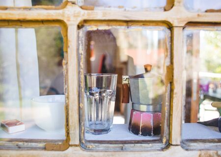 An old scratched geyser coffee maker is standing near the window. Glass and geyser coffee maker on the windowsill of an old wooden house.の写真素材