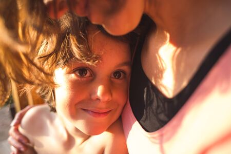 Portrait of a child hugging a mother, a boy spends time with mom, a woman gently hugs her son. Cute boy looks at his beloved mother. Sunset light passing through the hair.の写真素材