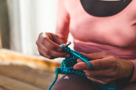 Woman crochets sitting in bed, Needlework during quarantine, The girl knits from thick blue yarn, Female hands close-up, Home hobby.の写真素材