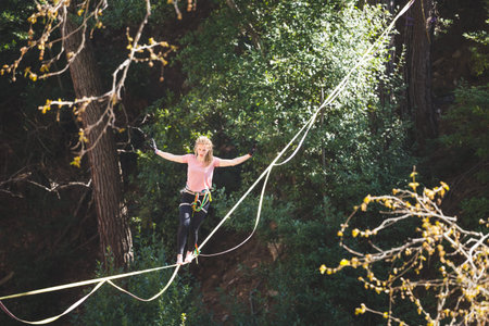 A woman is walking along a stretched sling. Highline in the forest. Woman catches balance....