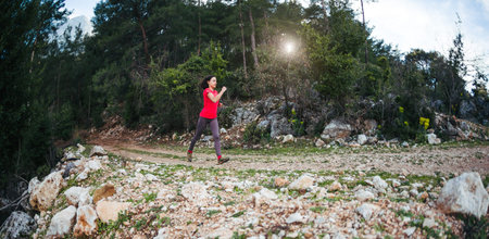 A woman runs along a mountain trail. Runner is training in the forest. Girl jogging in the park....