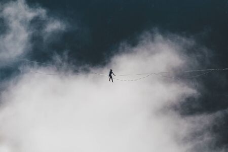 Highline on the background of the mountains. A woman sits on a stretched sling. Performance of a tightrope walker. Highliner balances over the abyss. The athlete is trying to get up after a fall.の写真素材
