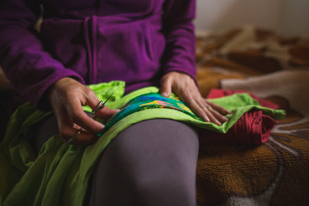 A woman sews a patch on torn clothes from an old sock, Restoration of clothing from improvised...