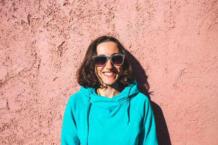 Portrait of a smiling girl in sunglasses on a pink wall background, A young woman is sitting near...