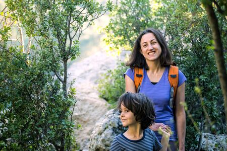 A woman walks with her son through the forest, The boy with his mother go hiking, A child with a backpack is in the park, Travel with children, The kid holds mom's hand, Mountain trail, Mothers Day.の写真素材