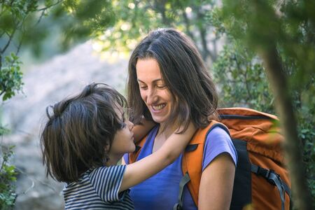 A child hugs mom for a walk in the forest. The boy congratulates mom on his mother's day. A woman with a backpack goes camping with her son. Portrait of a mother with her son.の写真素材