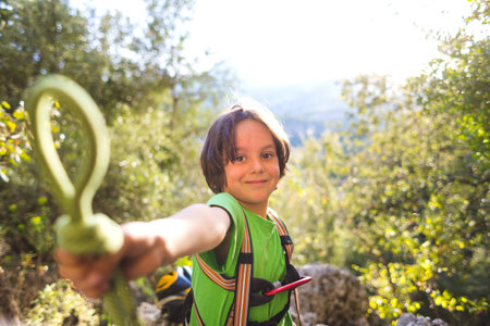 A child learns to knit the safety knot from the rope. Climbing rope and carabine for belaying. A little boy is trying to tie a knot. Scout training. Children's hands and safety rope. Teaching children.の写真素材